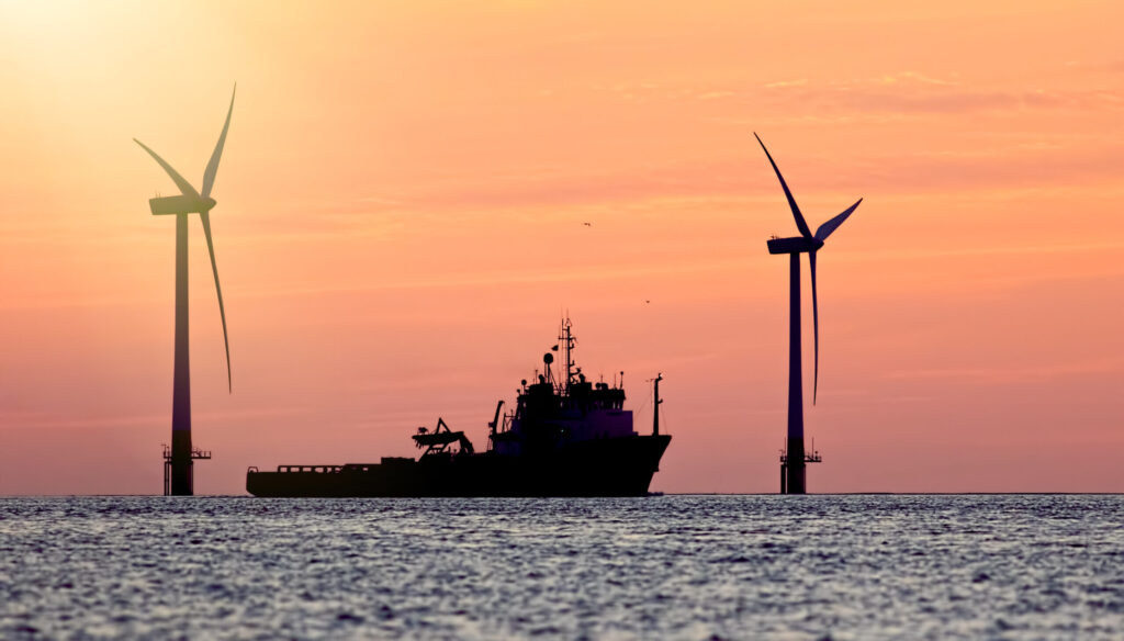 Sustainable resources. Wind farm with ship silhouette at tropical sunrise or sunset. Solar and wind energy and food supply represented.