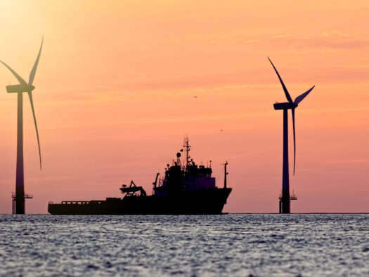 Sustainable resources. Wind farm with ship silhouette at tropical sunrise or sunset. Solar and wind energy and food supply represented.